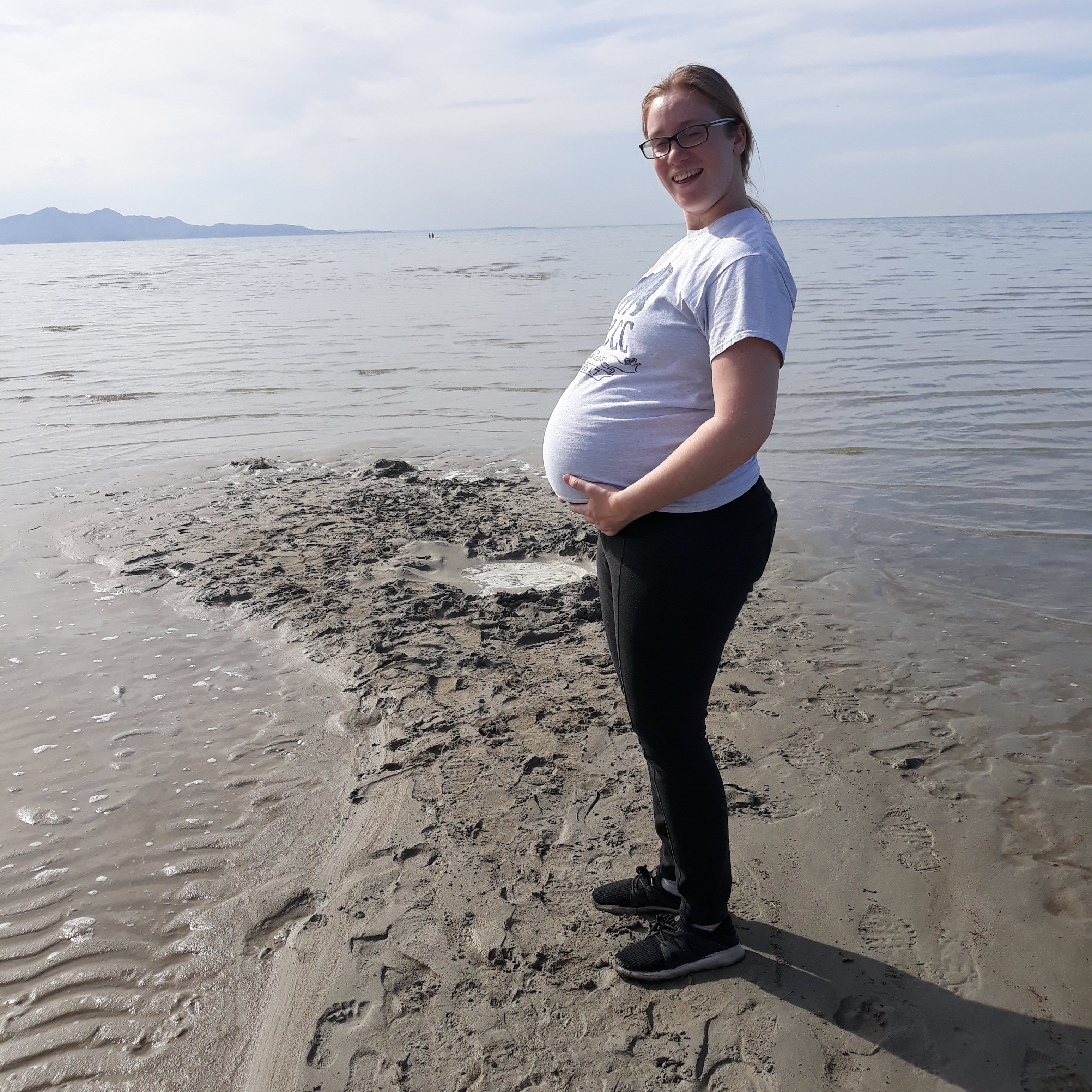 Pregnant women standing on a sandy beach with a clear sky