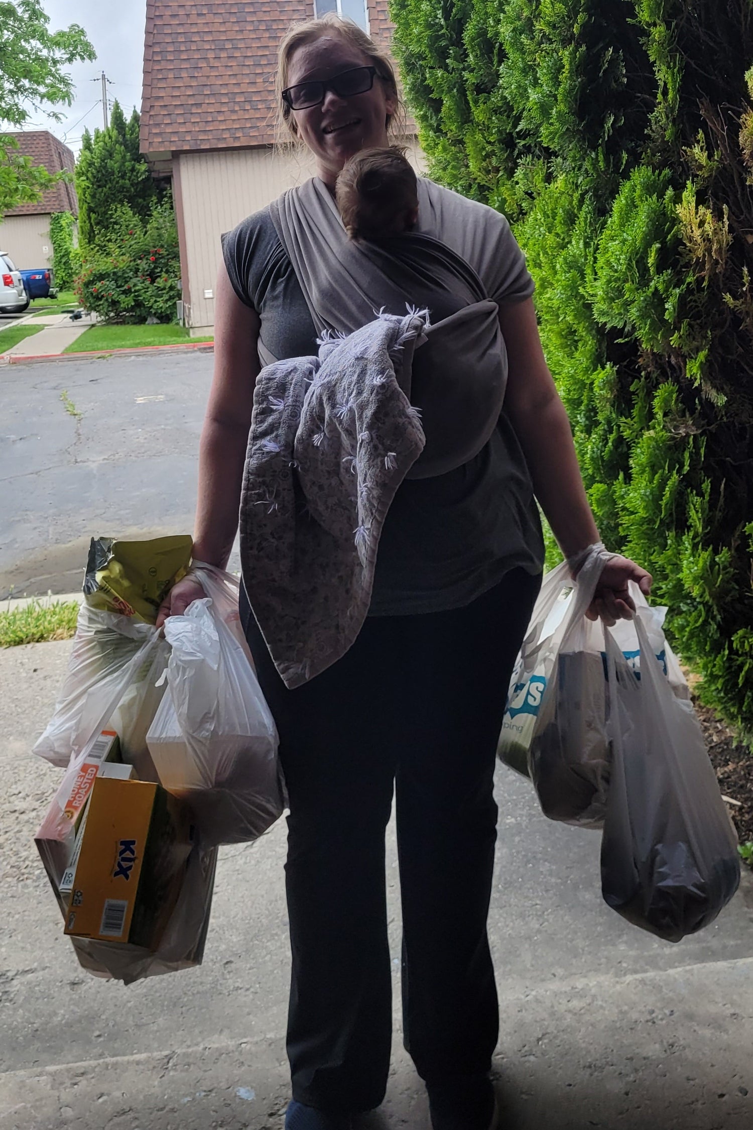 Mom holding a plastic bag with groceries and babywearing on a street