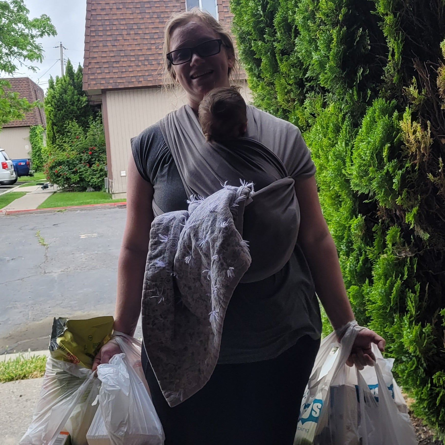Mom holding a plastic bag with groceries and babywearing on a street