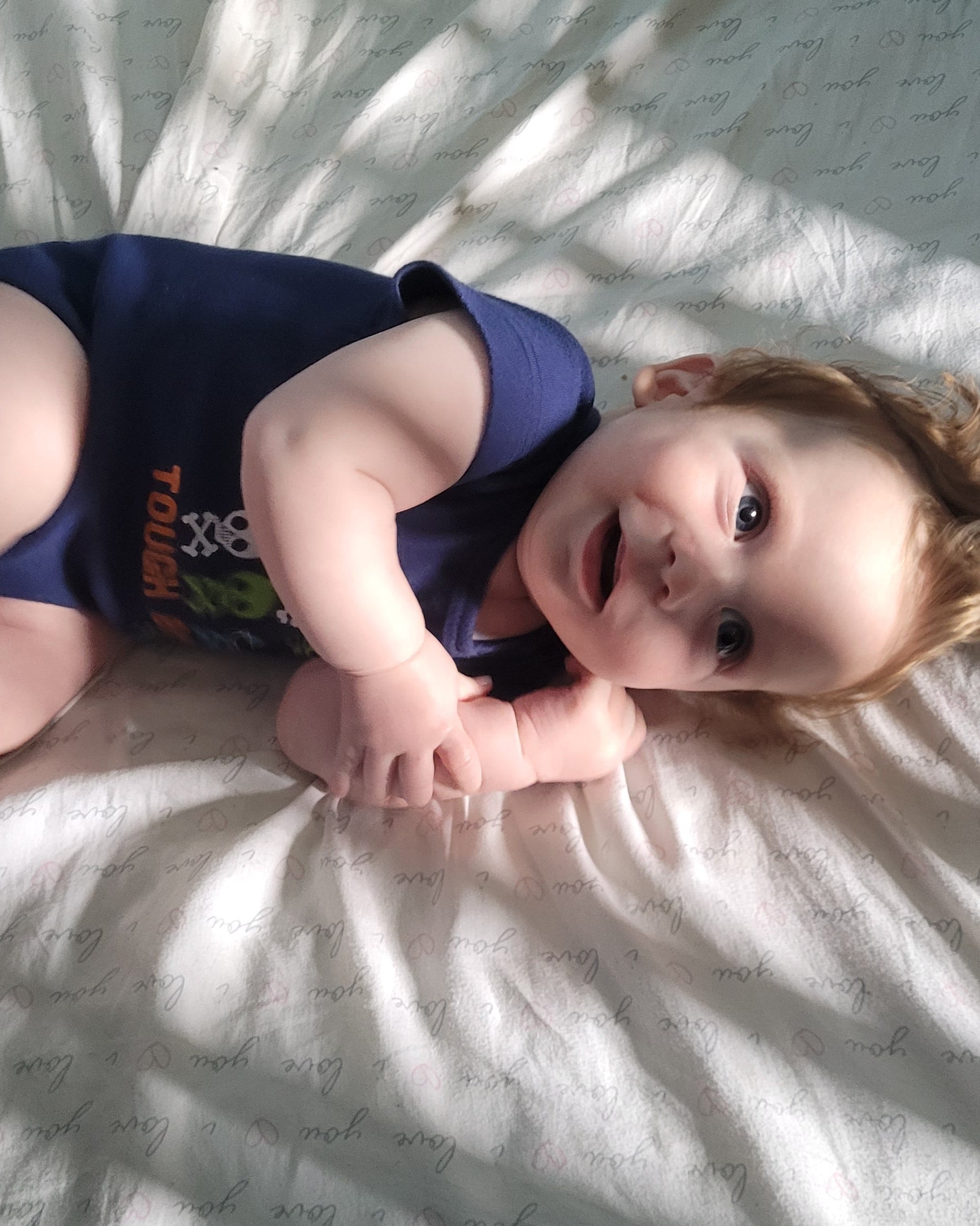 Baby laying on a white blanket with sunlight casting shadows