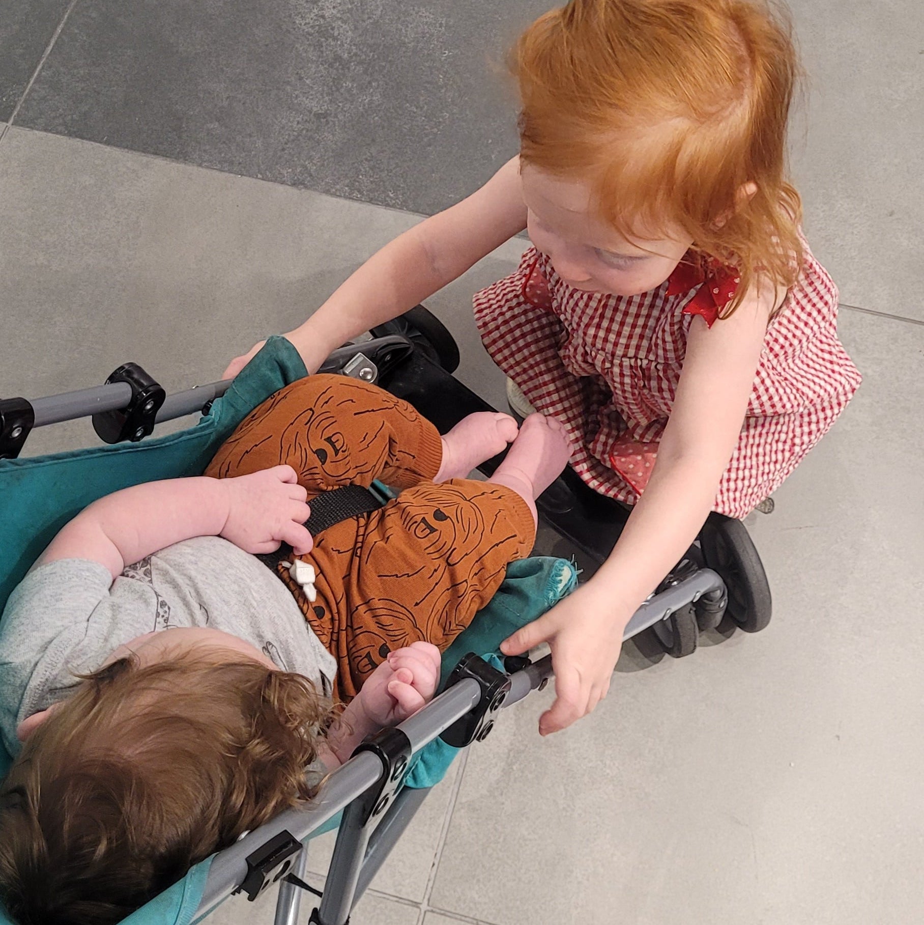 Child pushing a stroller with a baby inside on a tiled floor