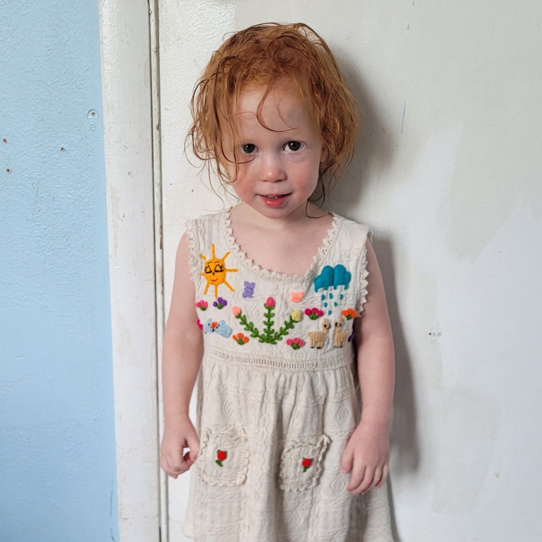 Child in a floral dress standing on a white surface with a wooden floor below.