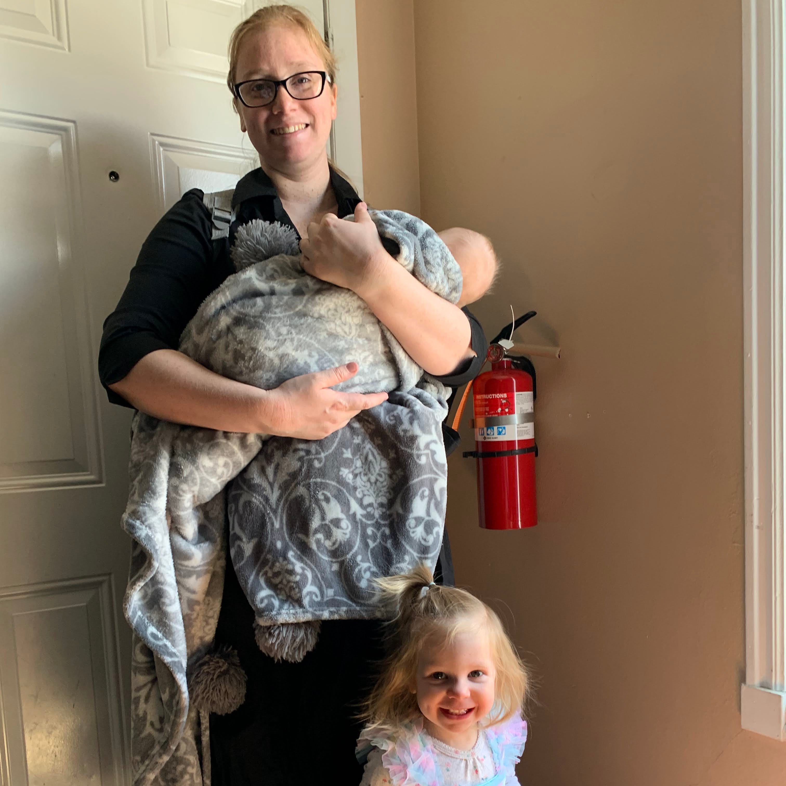 Two children, one in a dress and the other in a onesie, standing on a door with a fire extinguisher above them.