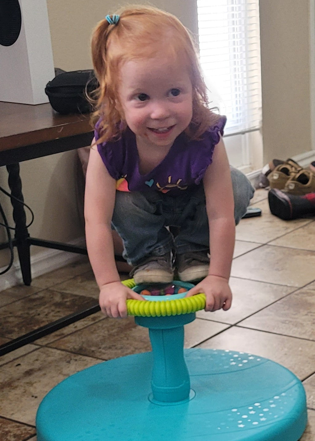 Child playing with a blue and green toy on a tiled floor.